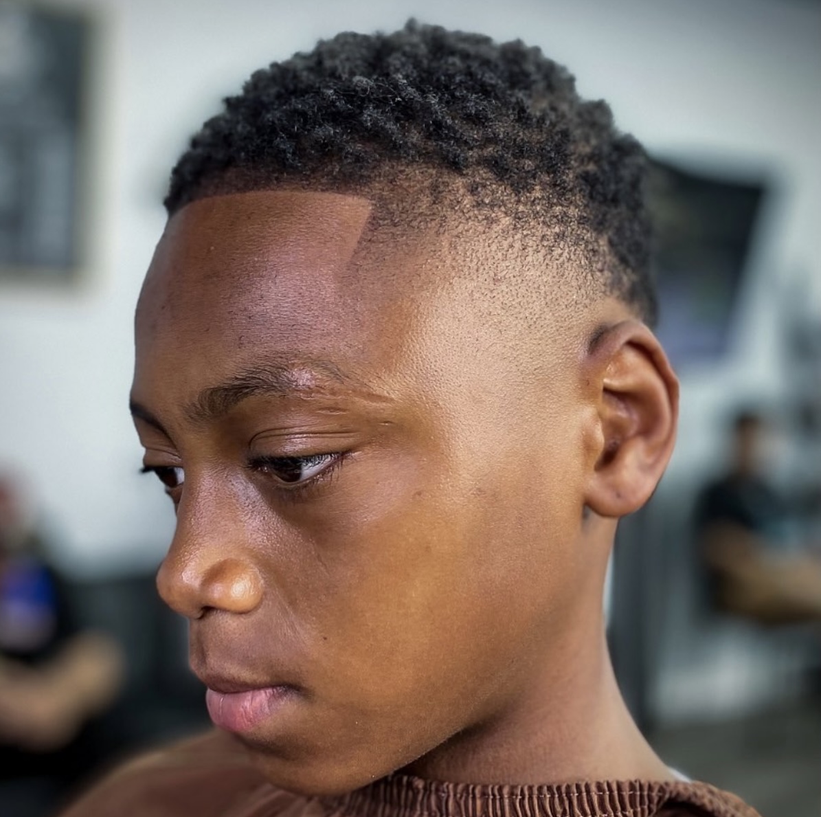 Side profile of a young boy with a curly top and a clean fade finished with a line-up