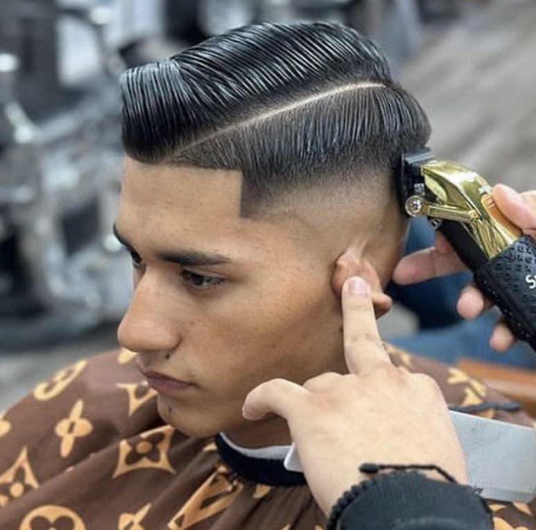 Man receiving a slick pompadour with a hard part and a skin fade